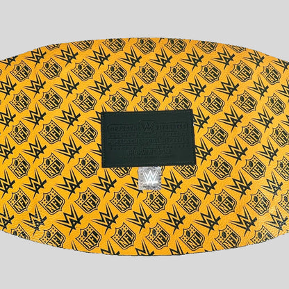 A yellow and black WWE-themed belt buckle featuring a repeating pattern of the WWE logo and NFL shield, with a black central brand plaque.