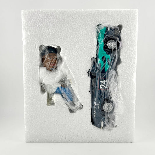 Styrofoam packaging containing two items, a bobblehead and a small blue car; photographed against light background.