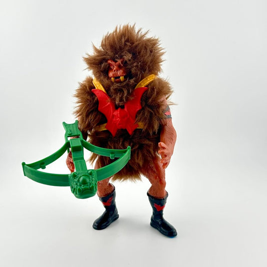 Toy figure of a creature with a furry brown coat and black boots, holding a green weapon on a white background.