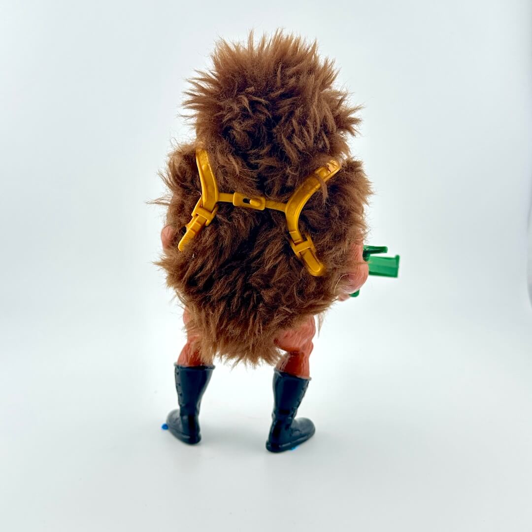 Action figure covered in brown fur, with black boots, standing next to green crossbow accessory. 