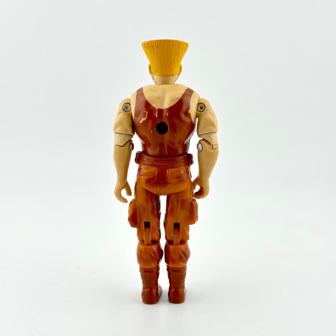 GI Joe/Street Fighter action figure in brown outfit and blonde flattop, photographed on white background. 