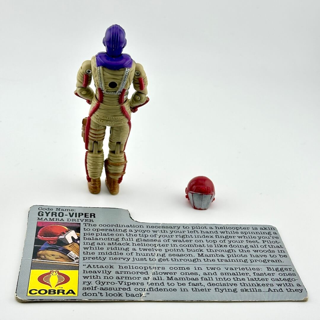 Action figure in flight suit with helmet and character card against white background. 
