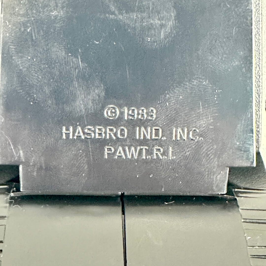 Close-up of a dark gray metal plaque with embossed text reading '© 1983 HASBRO IND. INC.