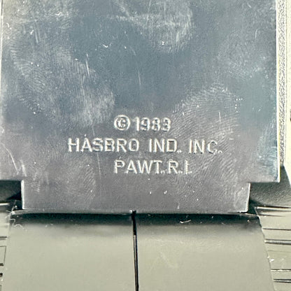 Close-up of a dark gray metal plaque with embossed text reading '© 1983 HASBRO IND. INC.