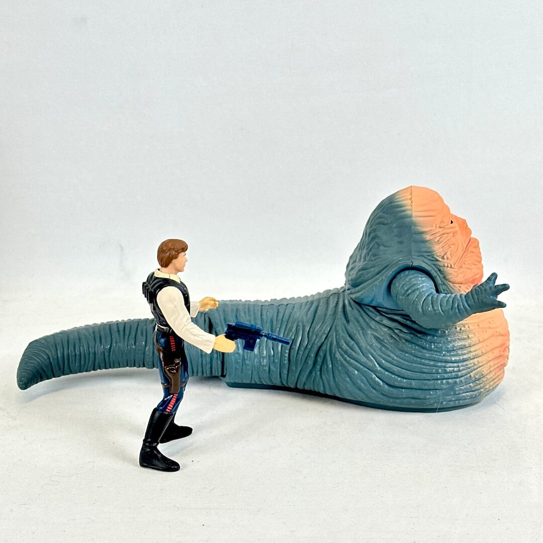 Toy figure of a character with a gun confronting a large, colorful creature on a white background