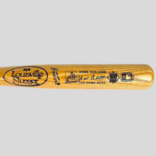Wooden baseball bat with burned in text and marker signature against gray background. 