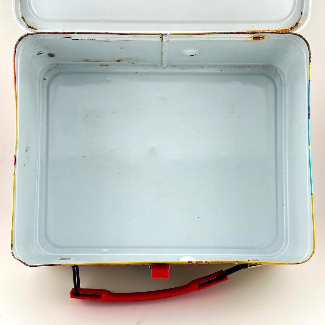 View of interior of metal lunchbox with some spots of rust but mostly white interior. 