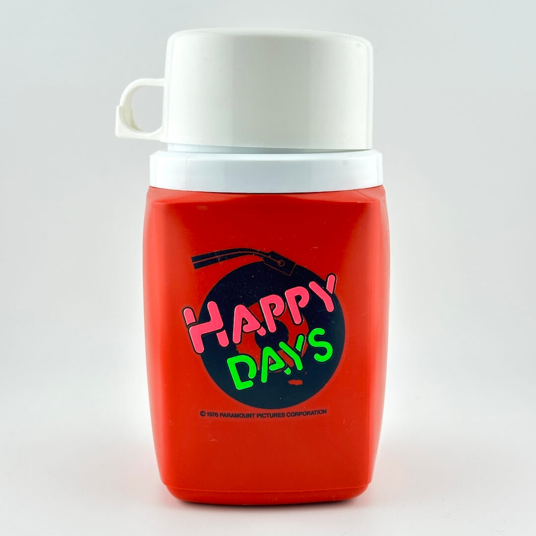 Red and white Happy Days thermos with logo printed on side, photographed on white background. 