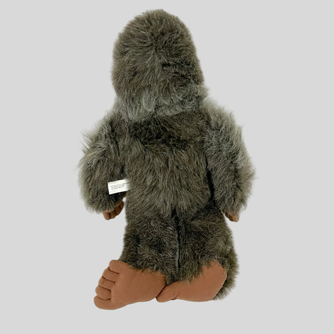 Plush toy resembling a creature with brown fur and feet on a white background