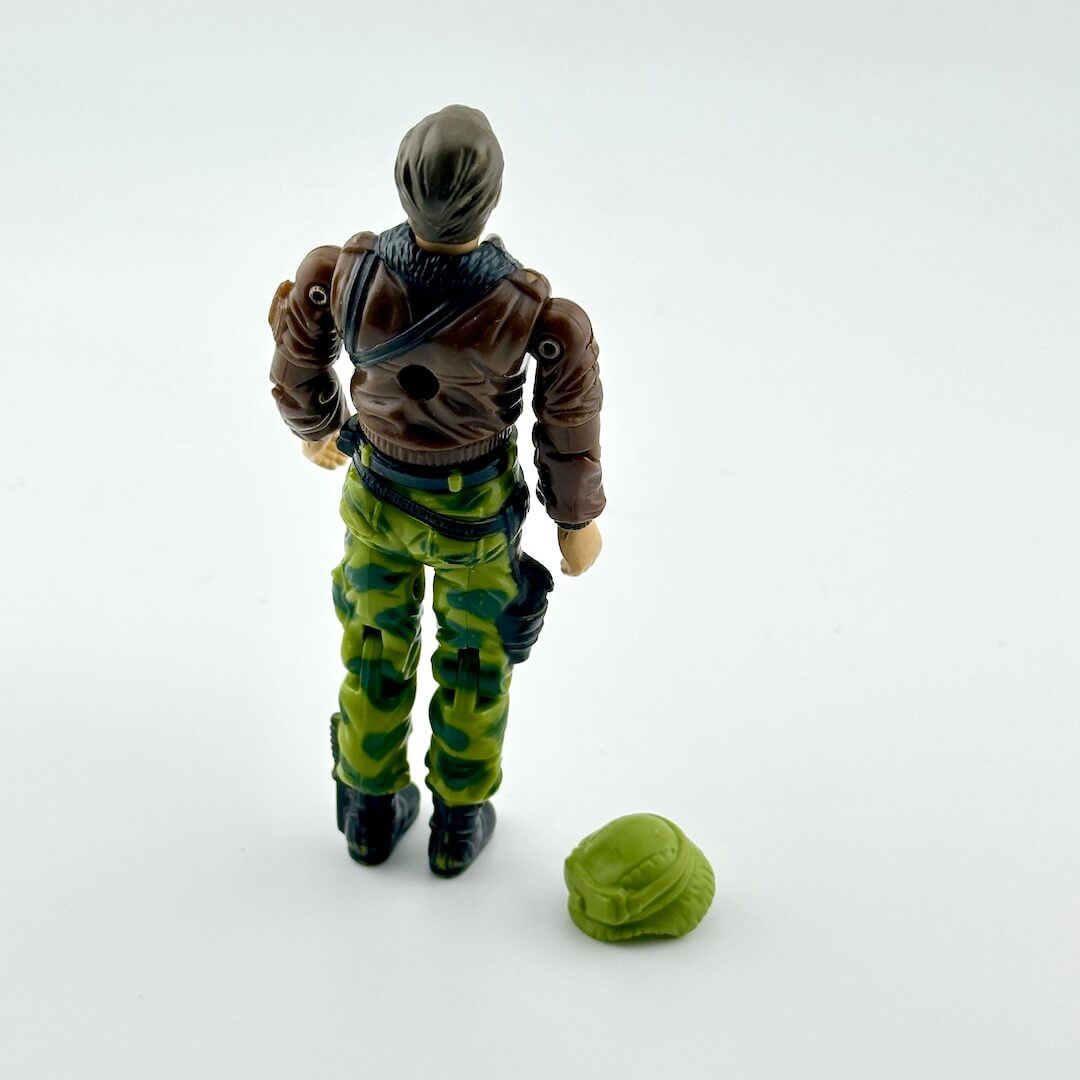 Action figure in camouflage pants and brown jacket with a green helmet on a white background
