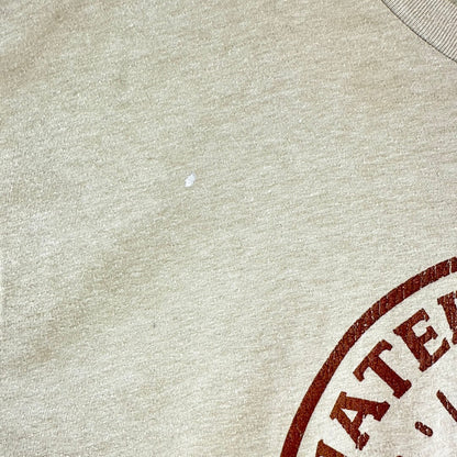 Close-up of a light beige heathered fabric with a partial dark red circular stamp graphic in the lower right corner.