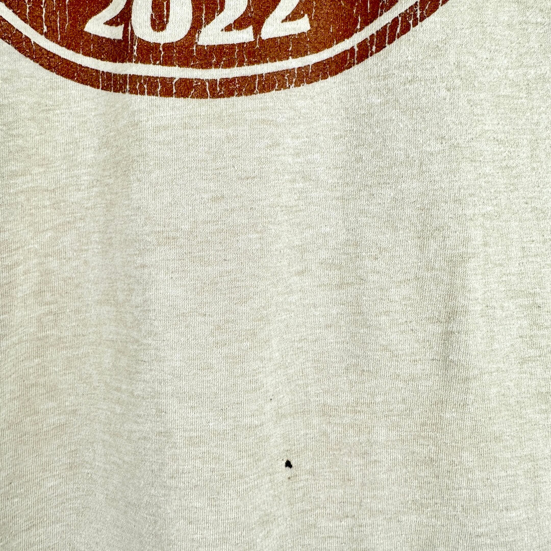Close-up of a light heather gray fabric with a distressed brown circular graphic at the top edge showing the number 2.