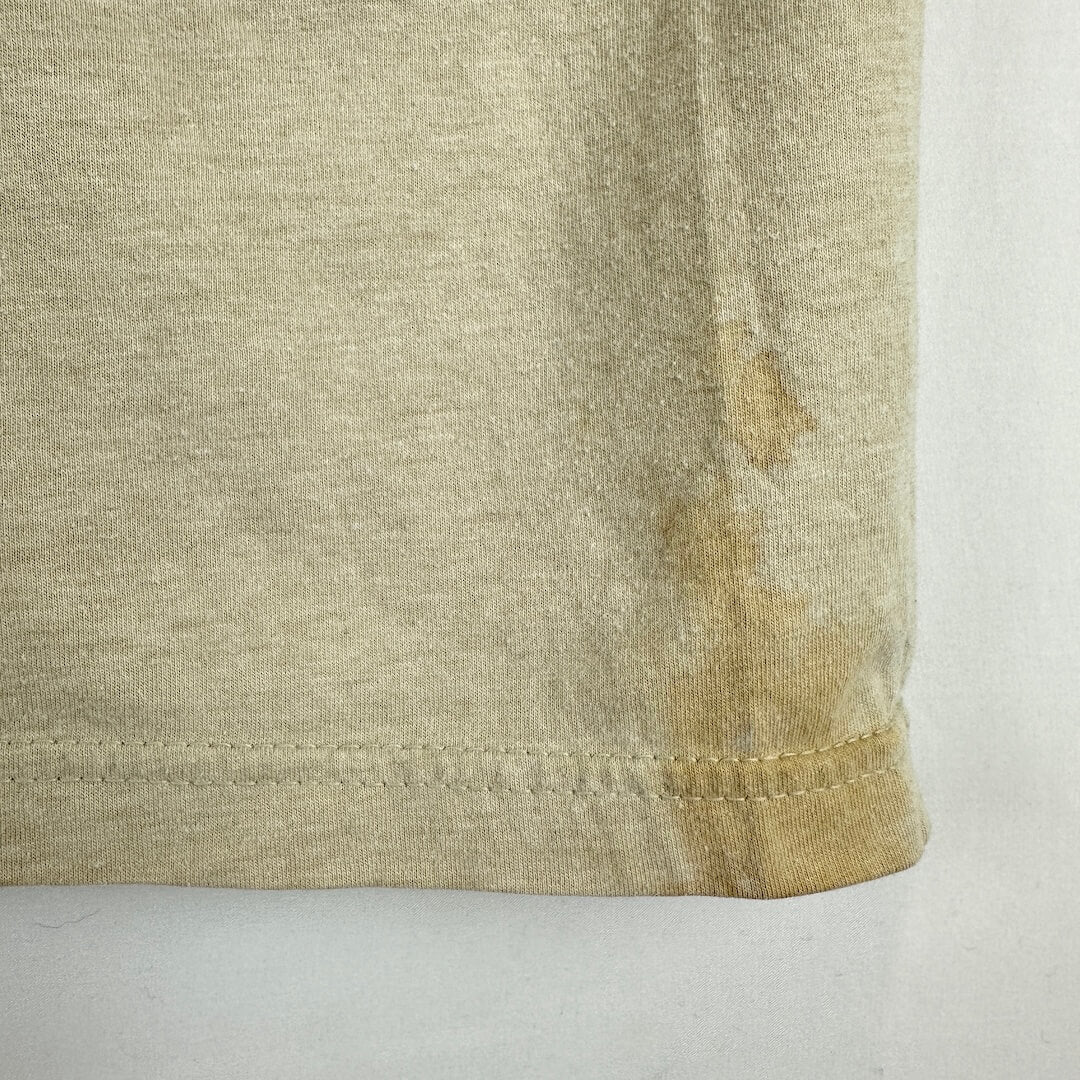 Close-up of a light beige or oatmeal-colored knit fabric corner with visible staining or discoloration near the hem.