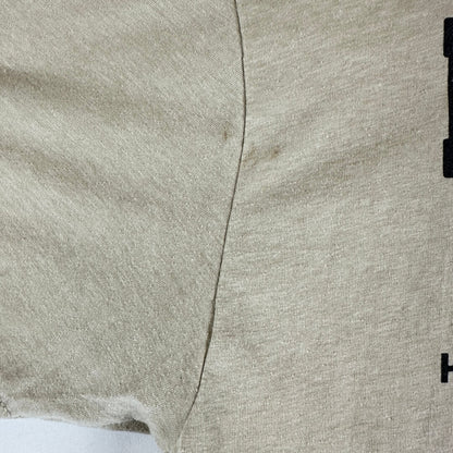Close-up of a light beige heathered fabric with a visible center seam and a small black printed detail on the right edge.