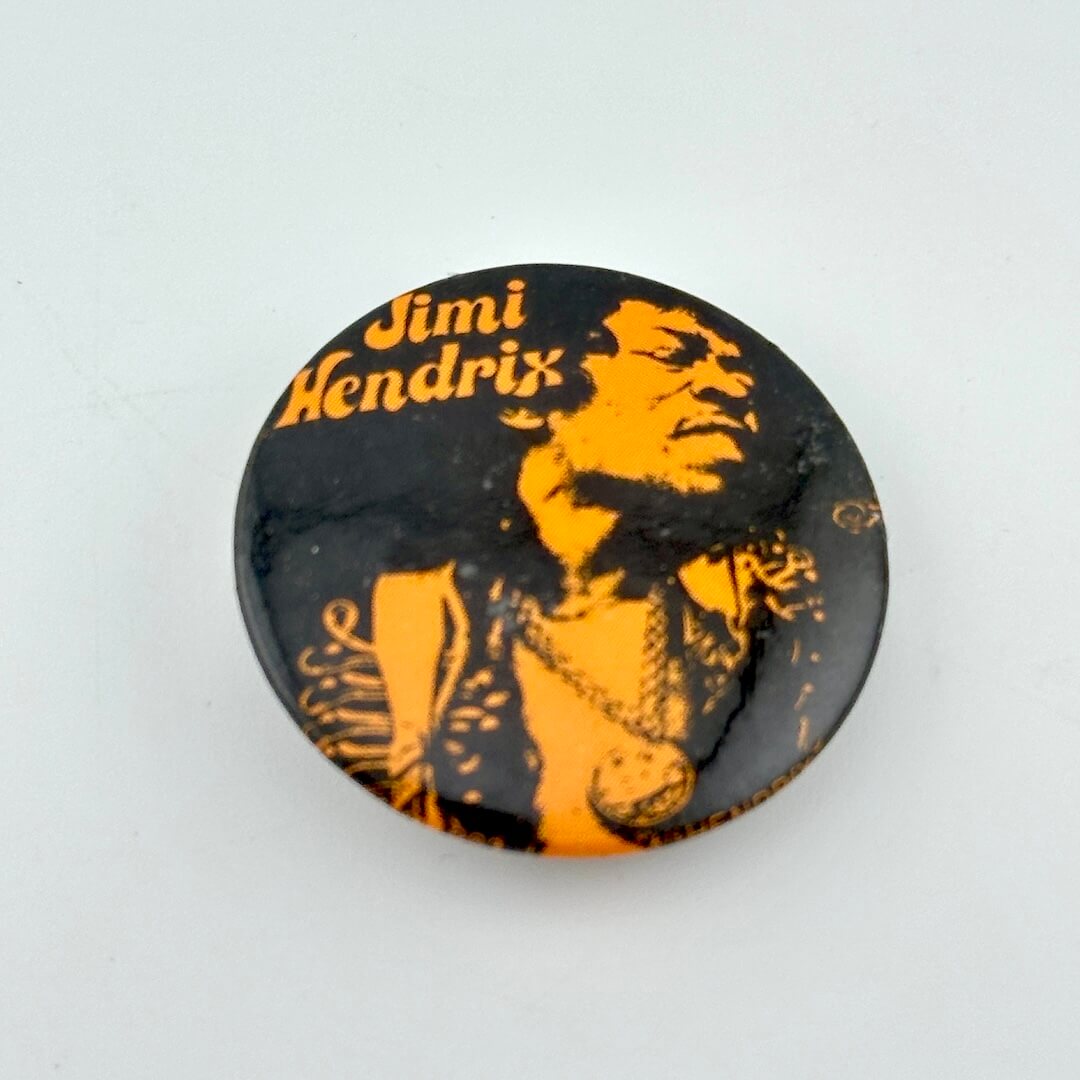 Circular pin with image of Hendrix and his name in orange. 