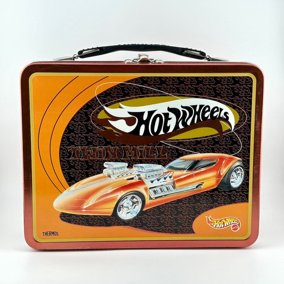 Hot Wheels themed metal lunch box with a black handle, featuring an orange & yellow custom car illustration & the Hot Wheels logo.