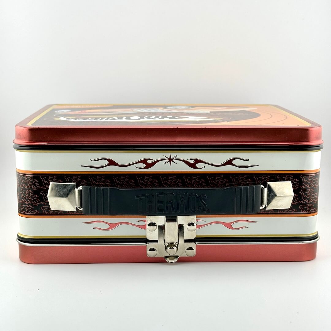 A rectangular metal lunchbox with a decorative design, featuring a red top and bottom, a white middle band.