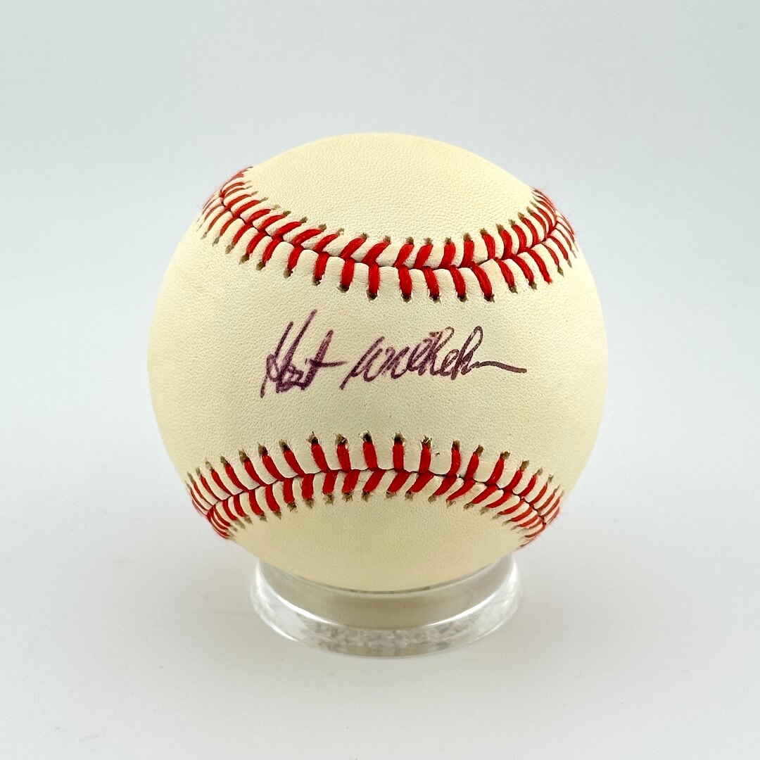 Baseball with red stitching on a clear stand against a white background