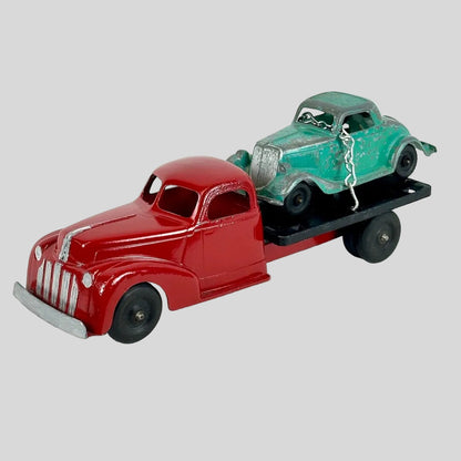 Model of a red truck with a green car on a flatbed trailer against a white background