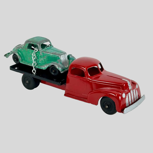 Red toy truck with a green car on its flatbed against a white background