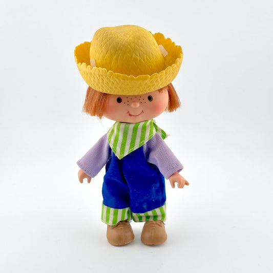 Toy figure with a yellow hat, purple shirt, blue pants, and green striped scarf on a white background