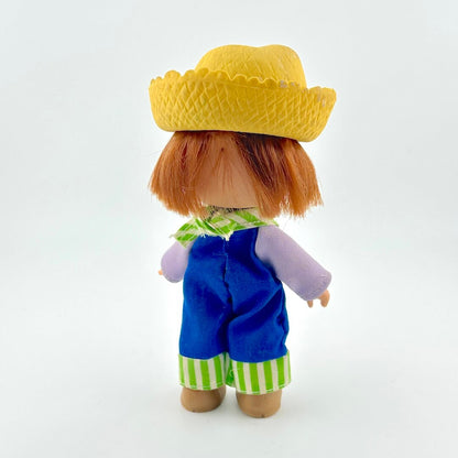 Toy figure with a yellow hat, blue overalls, and striped green and white pants on a white background