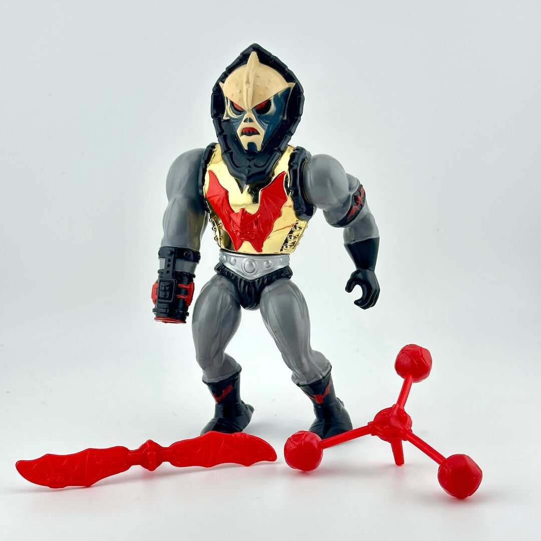Toy figure with a red and gray outfit, gold chest armor, and two red accessories on a white background