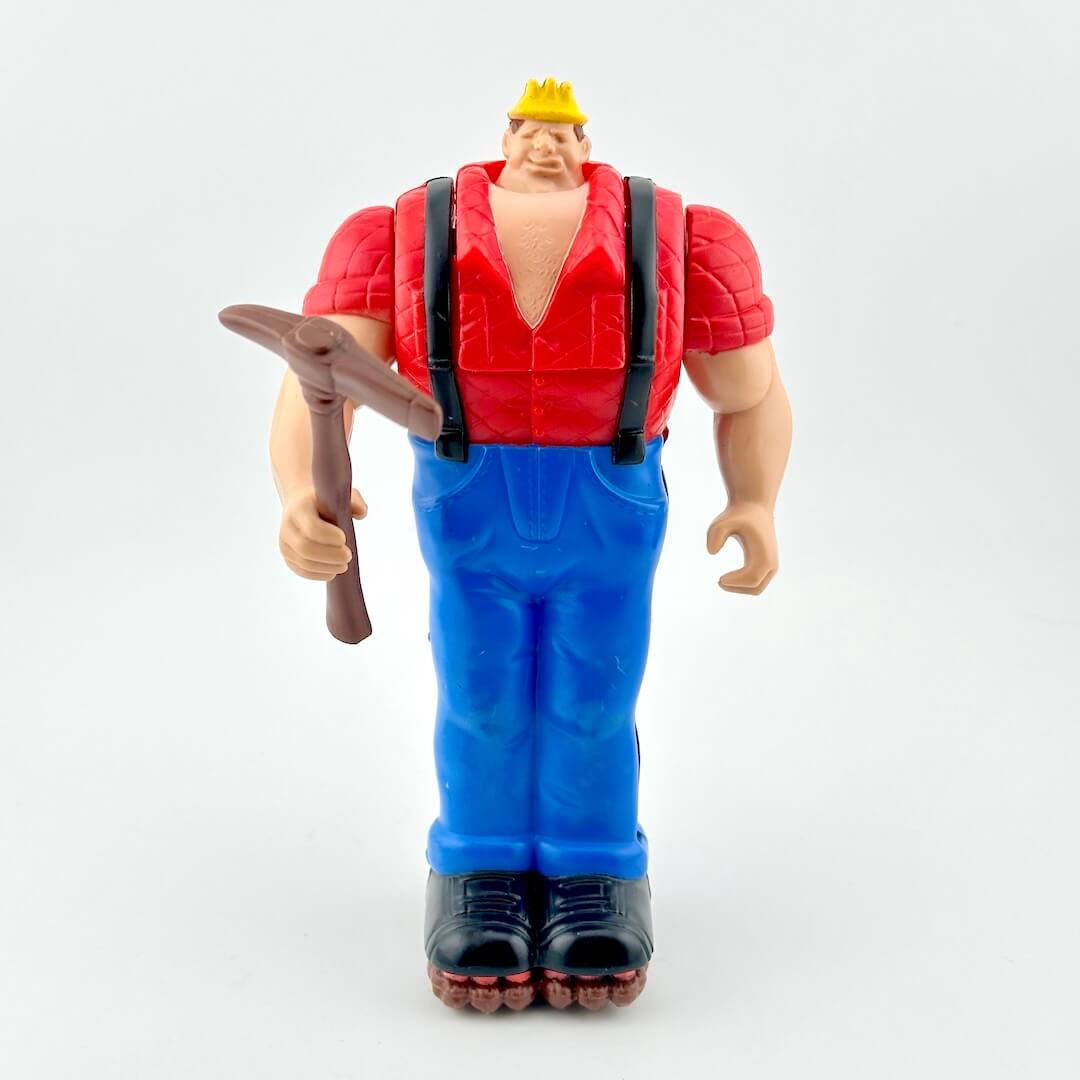 Toy figure in red shirt and blue pants holding brown tool against white background. 