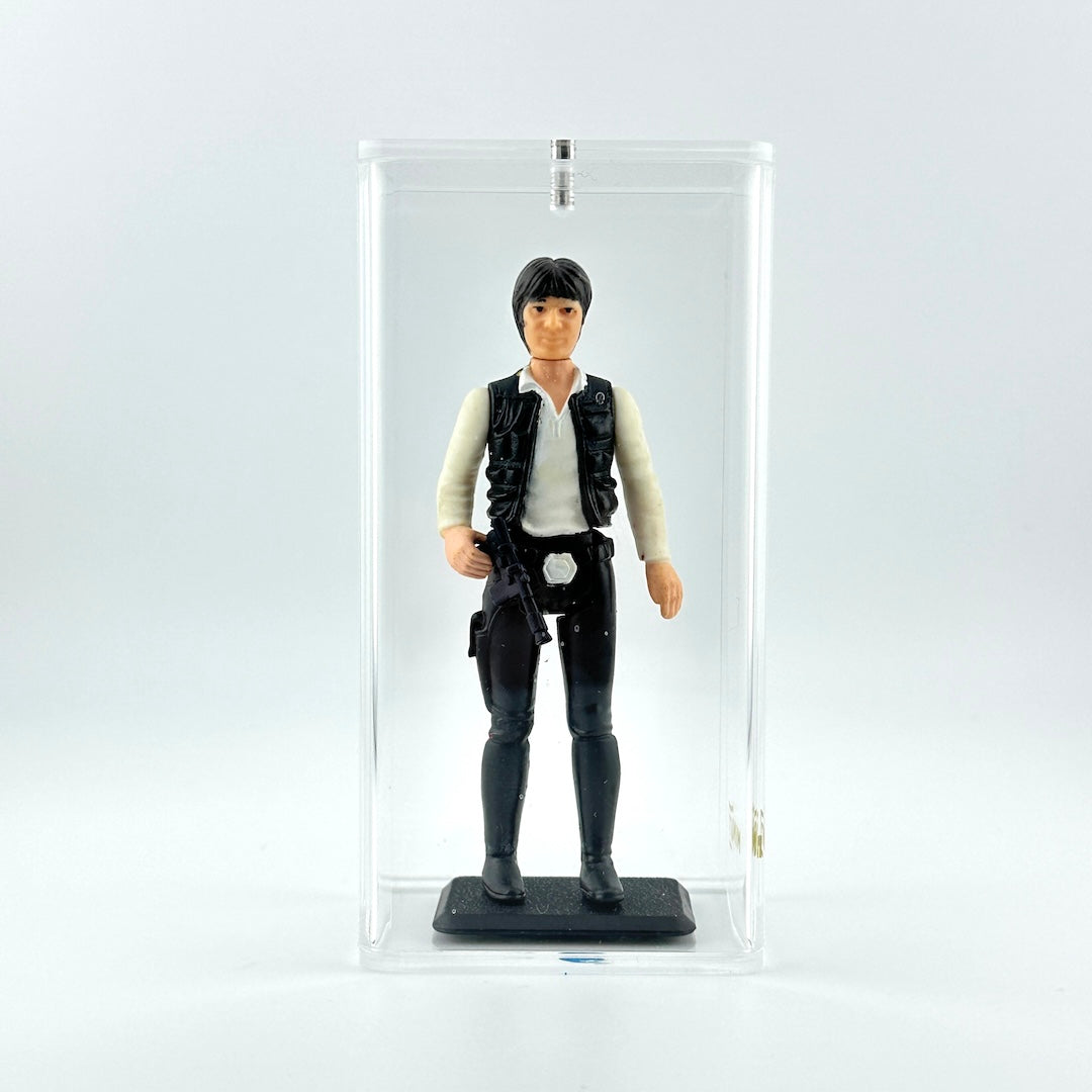 action figure in black pants and vest with white shirt and black gun against white background in clear display case.