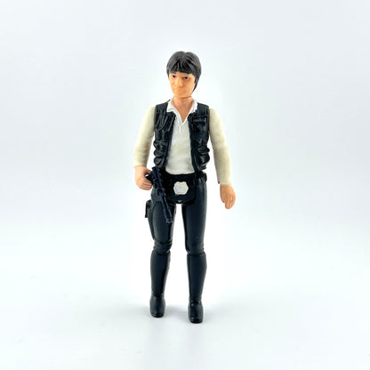 action figure in black pants and vest with white shirt and black gun against white background. 