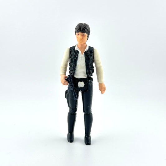 action figure in black pants and vest with white shirt and black gun against white background. 
