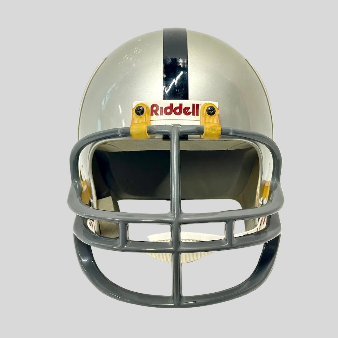 A Riddell football helmet in silver and gray with a black stripe down the center, yellow ear pads, and a gray faceguard.