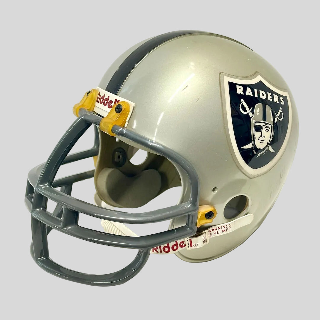 An Oakland Raiders football helmet by Riddell, featuring a silver and black shell with the team logo on the side.