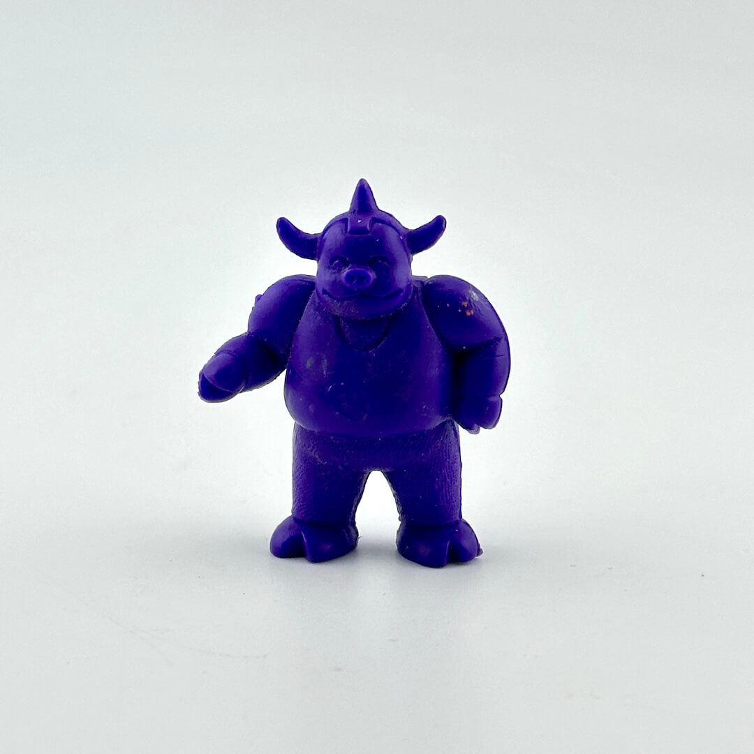 A small purple cartoon monster figurine with horns and a snout, standing on a plain light gray background.