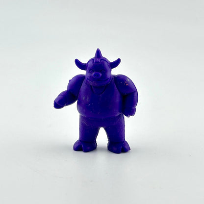 A small purple cartoon monster figurine with horns and a snout, standing on a plain light gray background.