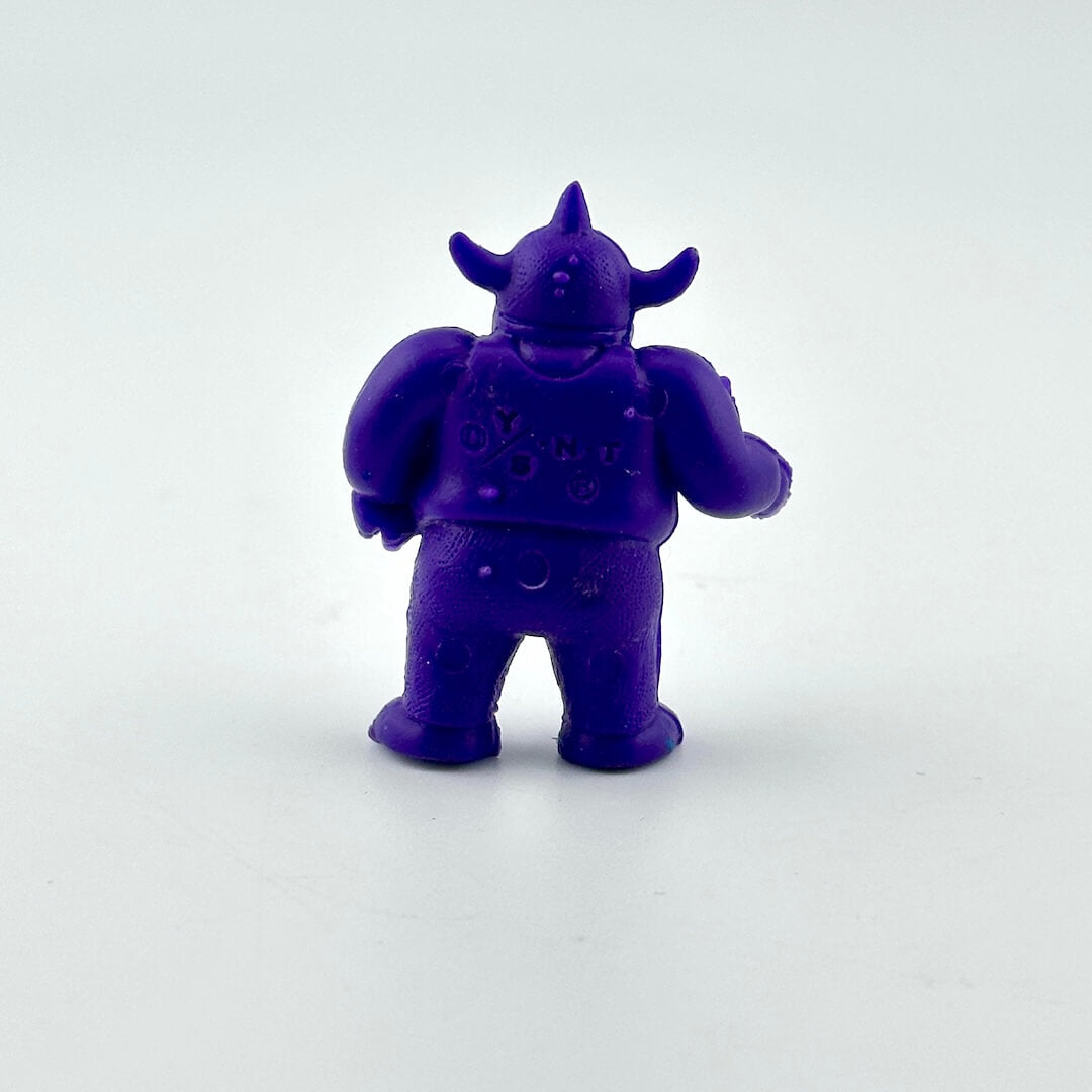 A small purple monster figurine shown from the back, standing on a plain light gray background.