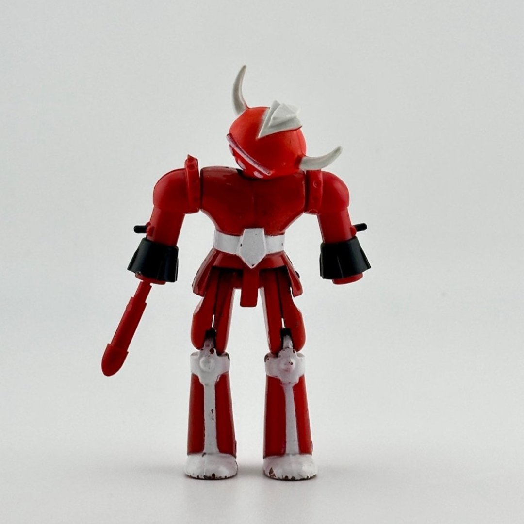 Image of red & white diecast robot with white bull horns & red attachment on left hand. White line & three dot detail on face.