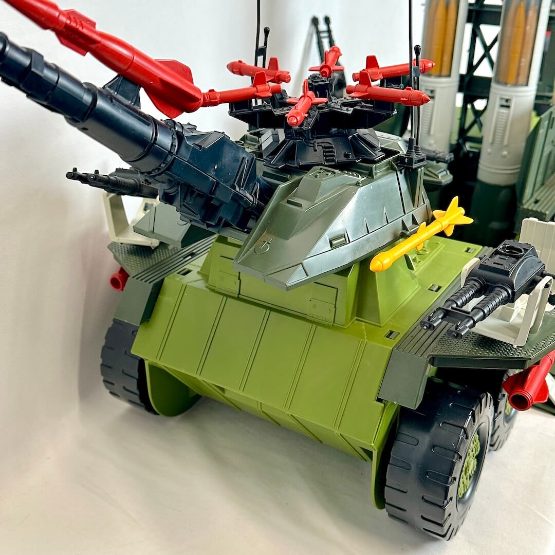 Toy vehicle with green body, black wheels, and red and yellow weapons on a white background