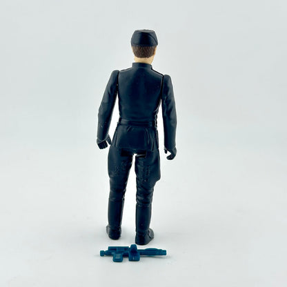 A vintage black plastic toy soldier figure shown from the back, wearing a uniform and standing next to a small blue accessory.