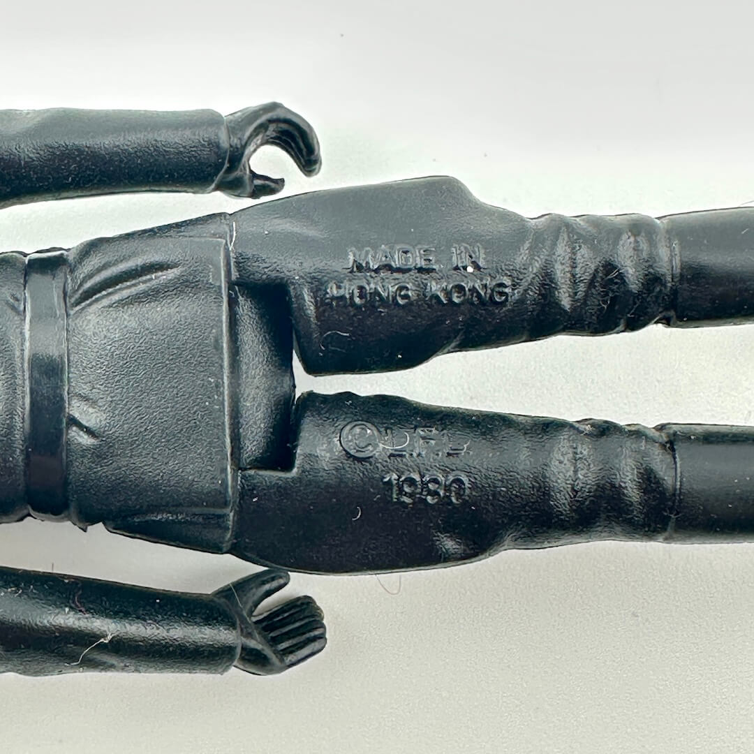 Close-up of a black plastic action figure torso and arms, showing embossed text reading 'MADE IN HONG KONG' 