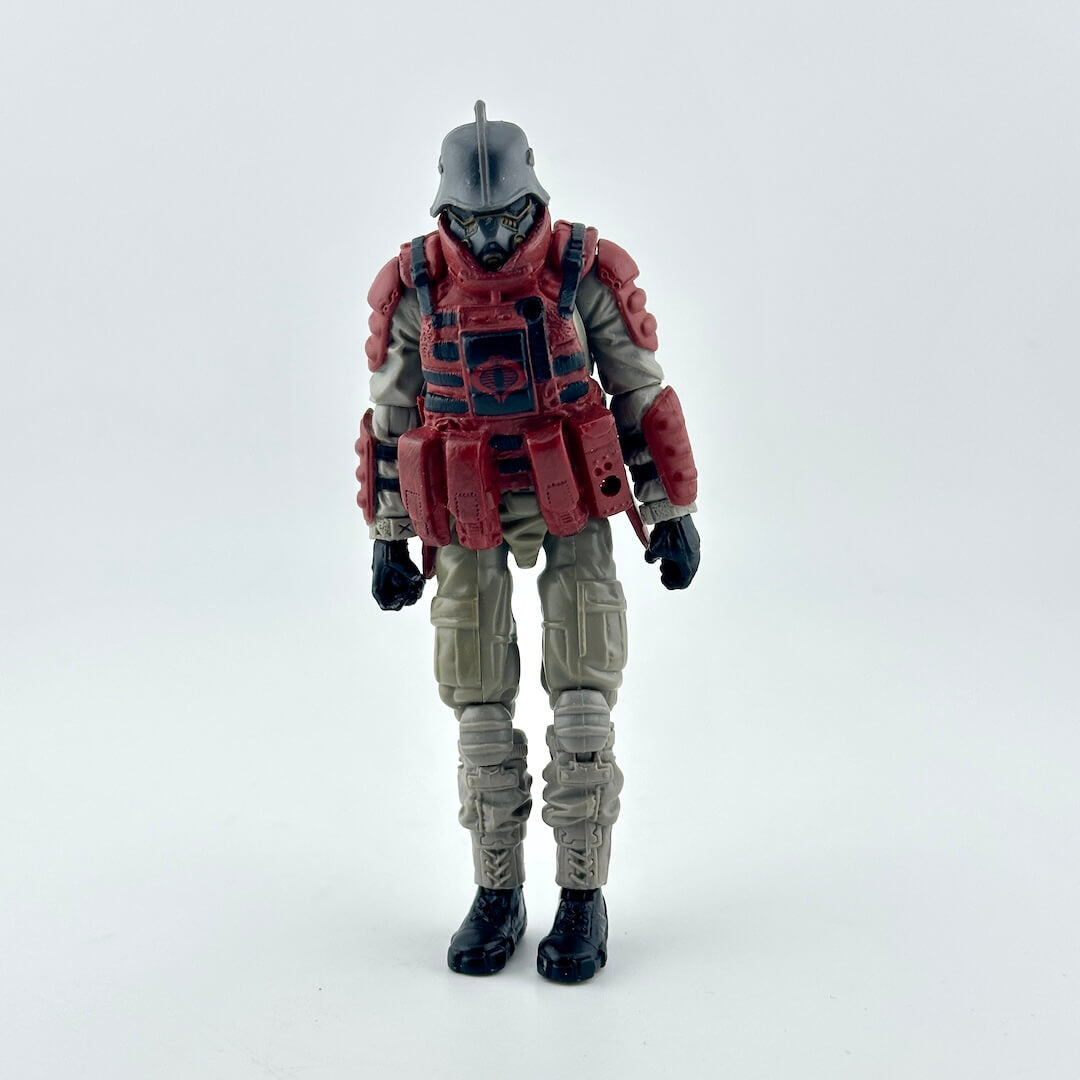 Action figure of a soldier in tactical gear, featuring a gray helmet, red armor plating, and beige combat pants.