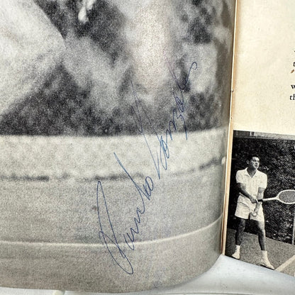 Close-up of a signature on a black and white photo of a person playing tennis in the background.