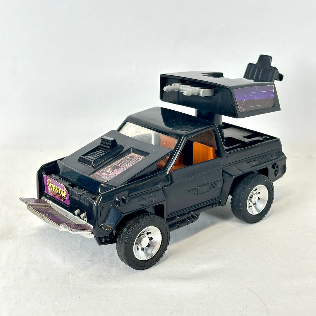 A black toy truck with a raised roof carrying a gun, featuring orange interior windows . 