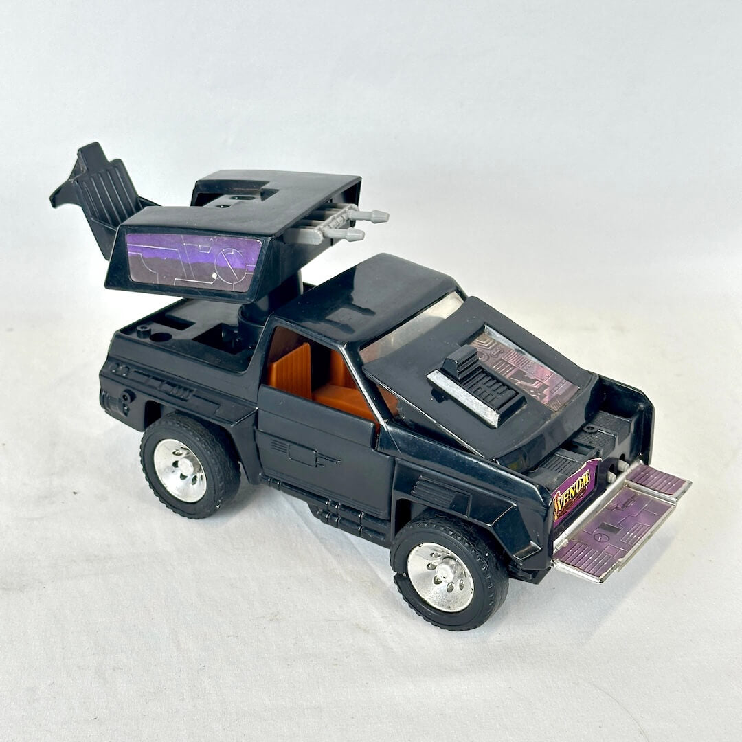 A black toy car with futuristic styling, an orange interior, and silver wheels, photographed on a light gray background.