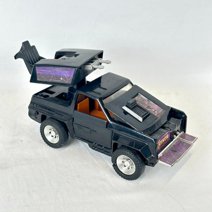A black toy car with futuristic styling, an orange interior, and silver wheels, photographed on a light gray background.