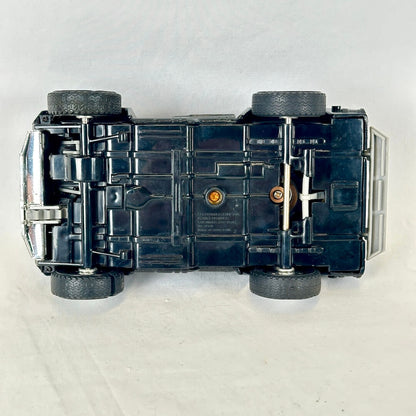 A vintage black toy car shown from a top-down view, lying upside down on a light gray fabric background.