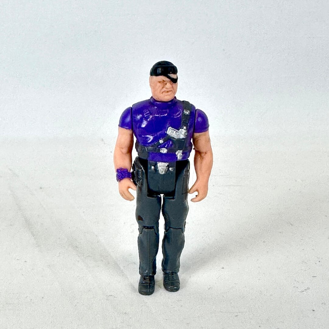 A vintage action figure of a muscular man with an eyepatch, wearing a purple shirt, black vest, and dark pants.