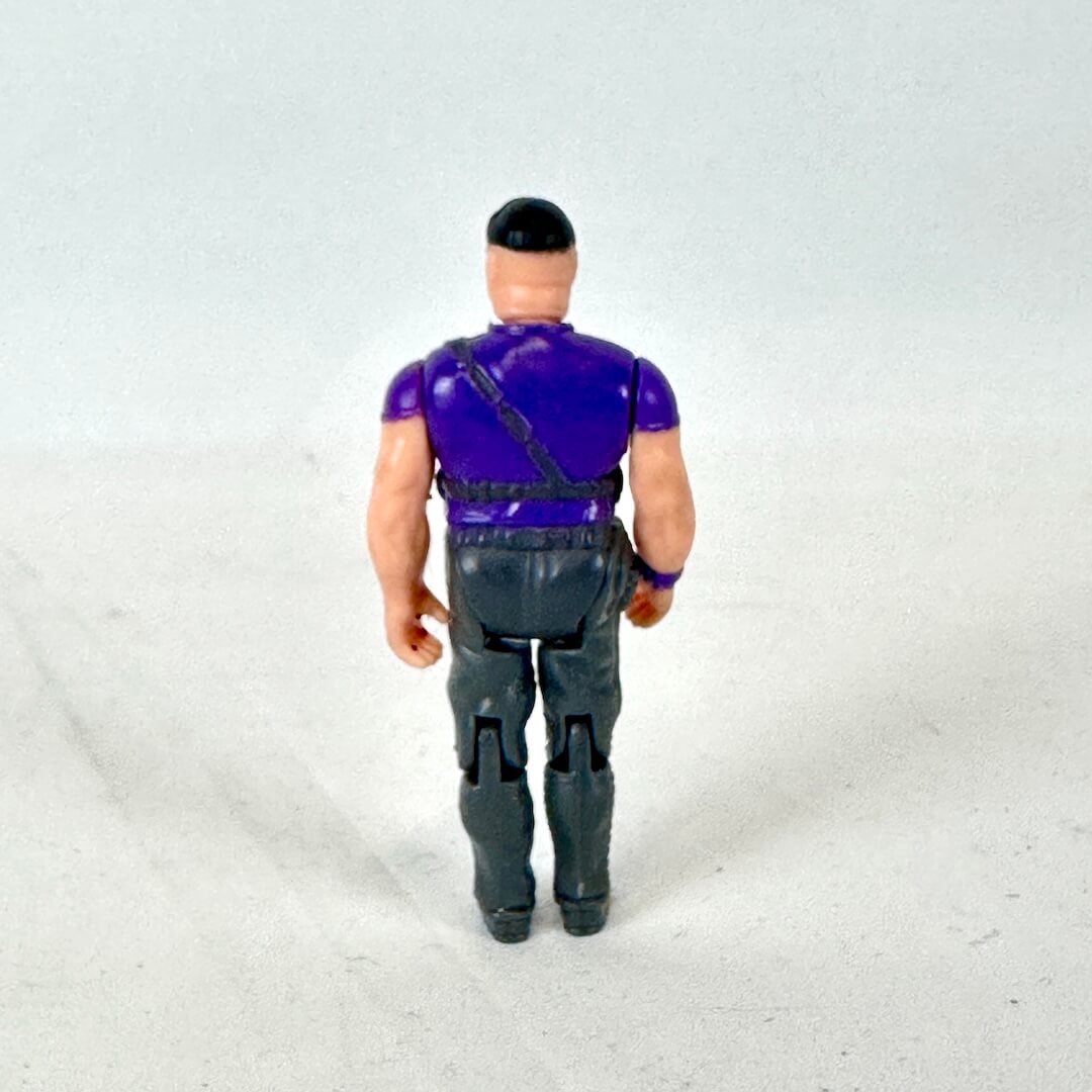 A vintage action figure shown from the back, wearing a purple shirt, dark gray pants, and a black cap.
