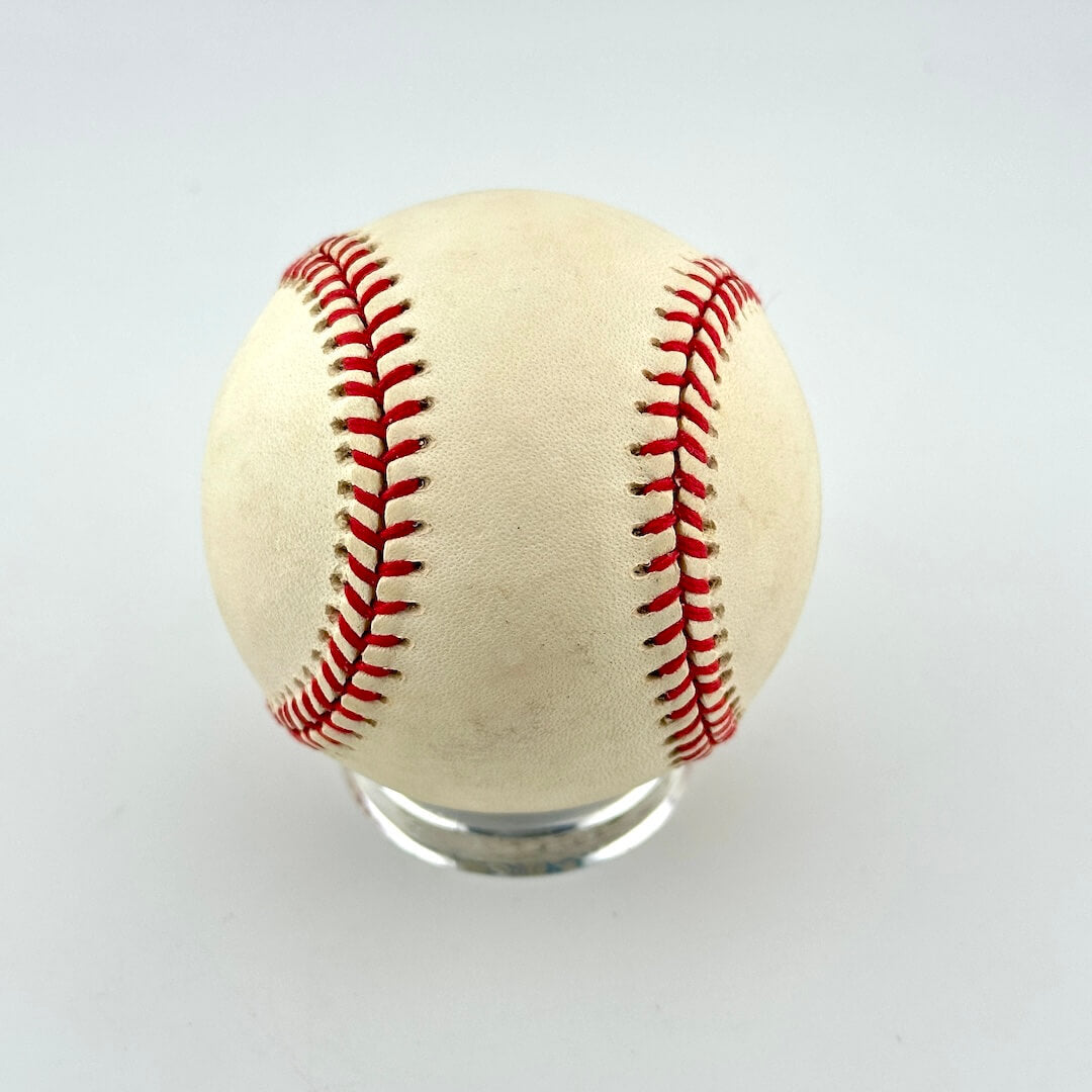 A single vintage baseball with red stitching and a weathered off-white leather surface.