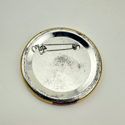 Backside of round pinback badge with yellow rim and silver metal back with bar attachment. 